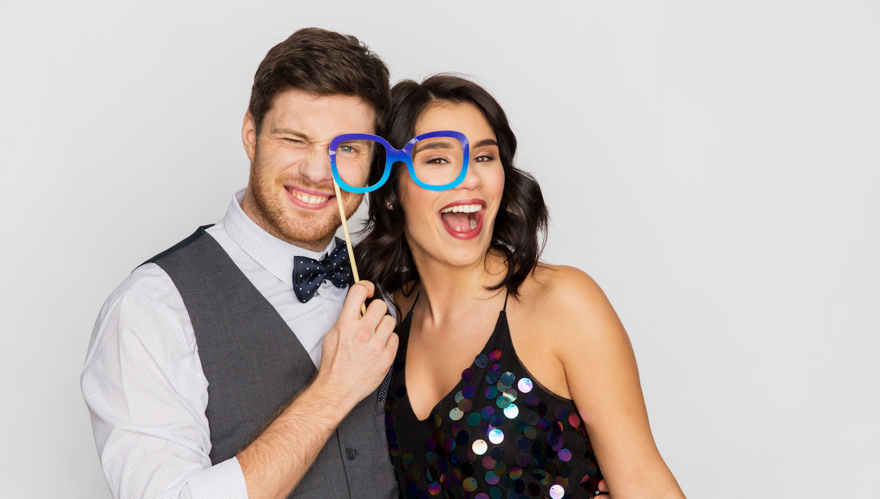 Smiling couple posing with oversized blue photo booth glasses at a party, perfect for a fun DIY wedding guestbook photo booth idea.
