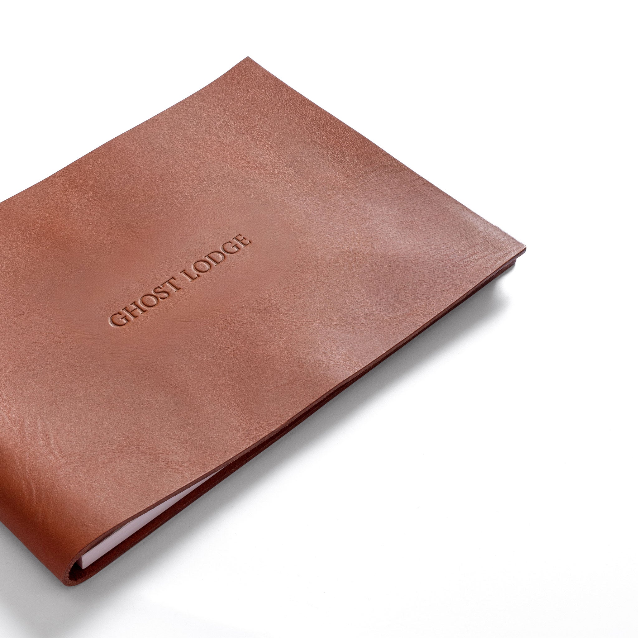 A tan leather guestbook cover or with 'GHOST LODGE' blind debossed on the front, photographed on a clean white background.