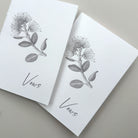 Two white vow books with pohutukawa floral illustrations and 'Vows' text on a gray background