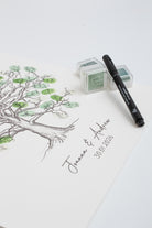 A white paper fingerprint guestbook featuring a black ink oak tree illustration with green leaf accents and the personalised names 'Jenna & Andrew' along with the date '30.01.26'