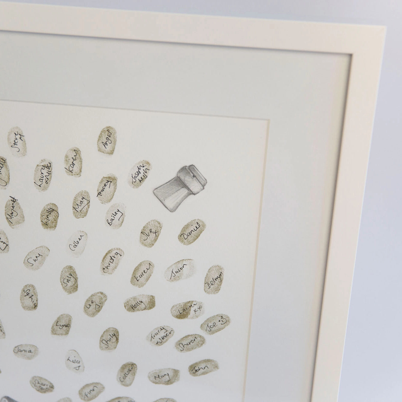 A framed fingerprint guestbook print featuring numerous small, hand-written guest names in muted beige and gold tones, with one larger sketch shaped like a champagne cork. The art piece is housed in a thick, clean white frame.