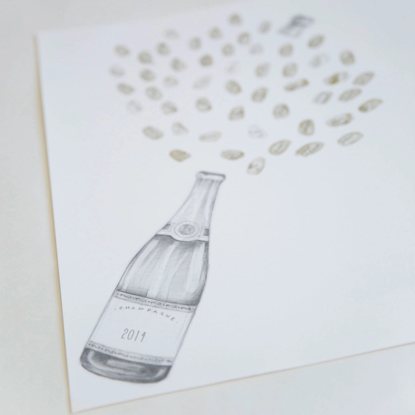 A guestbook retirement print featuring a hand-drawn champagne bottle with 2014 on the label, with scattered champagne bubble fingerprints forming a fountain shape above it. The print is shown at an angle on a light table surface.