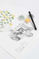 A custom fingerprint wedding guestbook with a vintage tractor design printed on white paper, styled with green and yellow ink stamps, a black pen, and two ink pads on a clean white background.